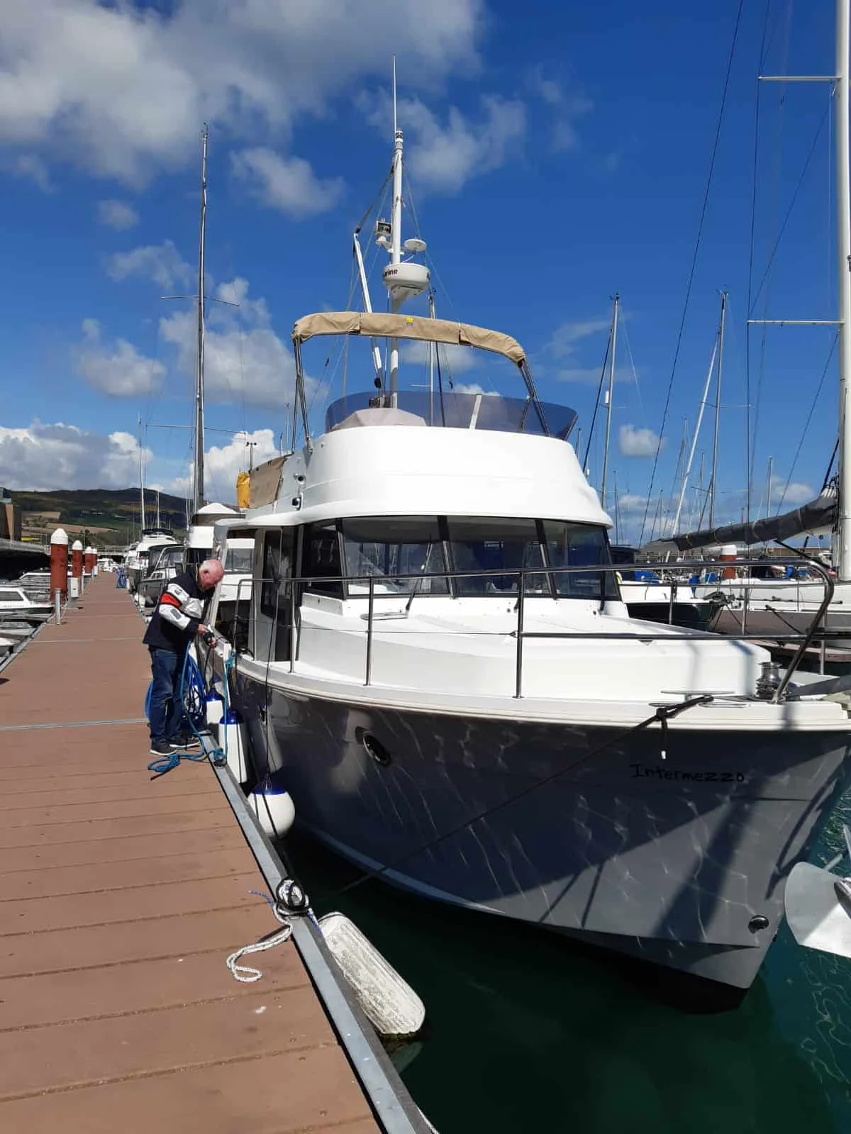 Motor yacht Intermezzo alongside a pontoon in Greystones, with the owner adjusting fenders.