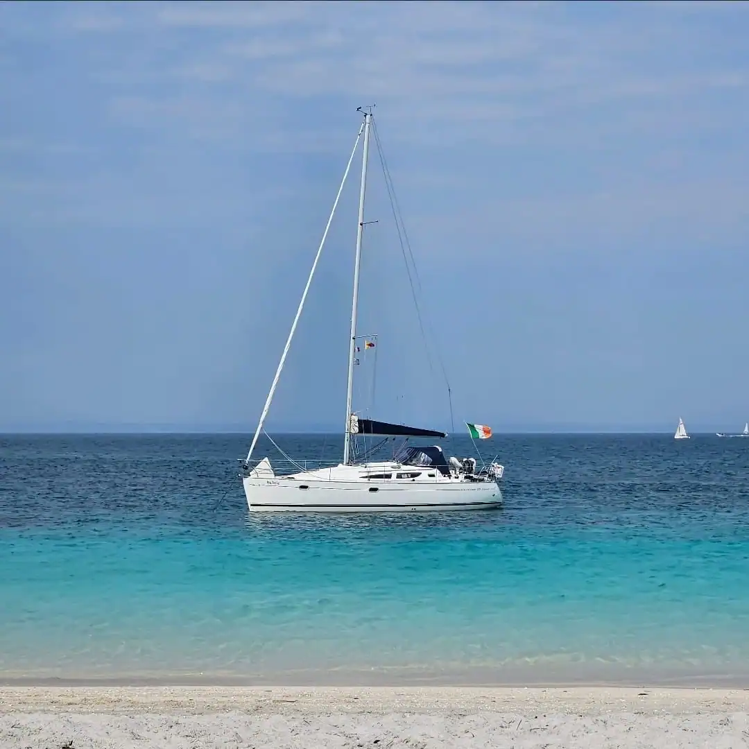 Sailing yacht anchored off a beach in sunshine